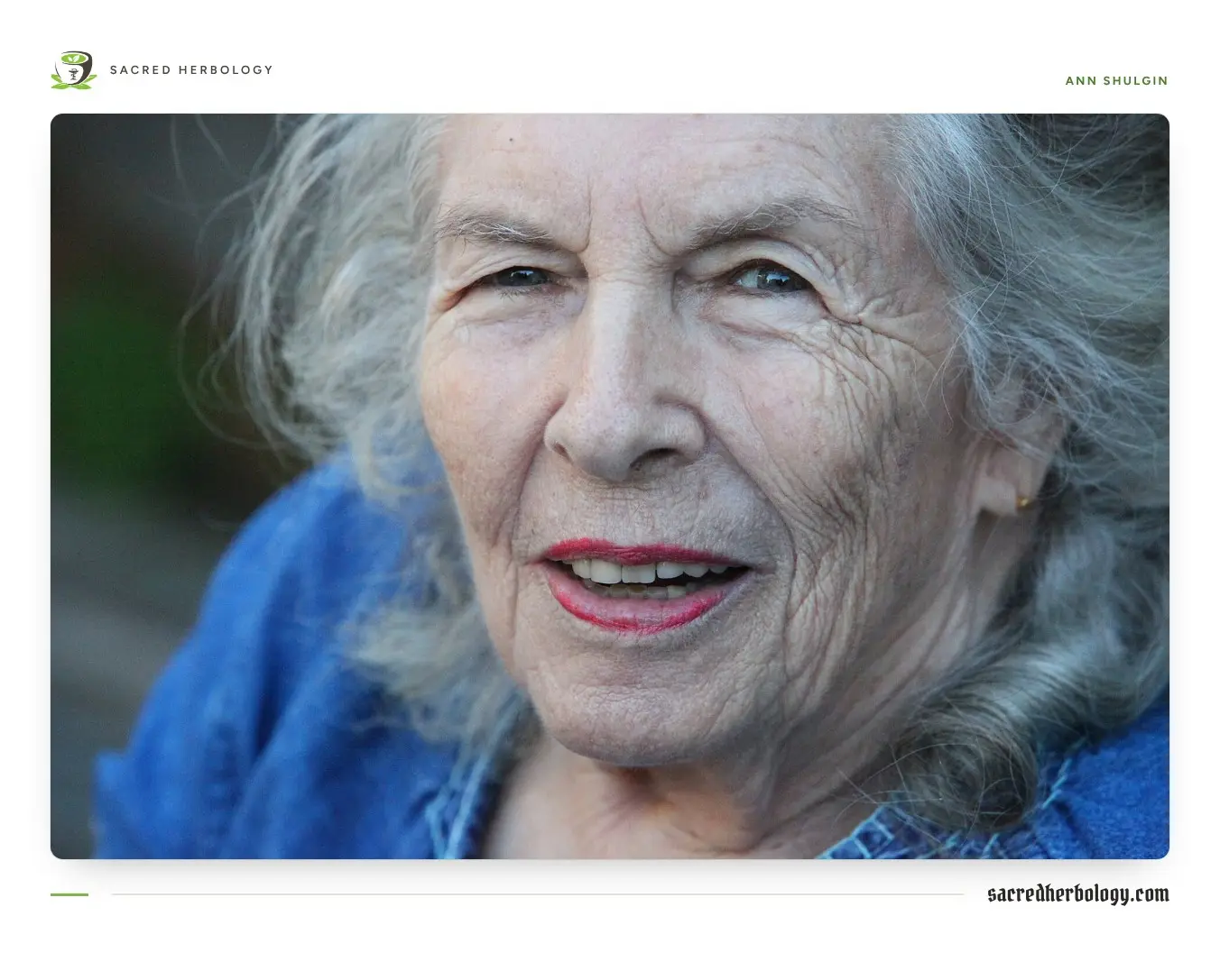 Close portrait of an older woman with long grey hair and red lipstick, smiling, in a denim jacket