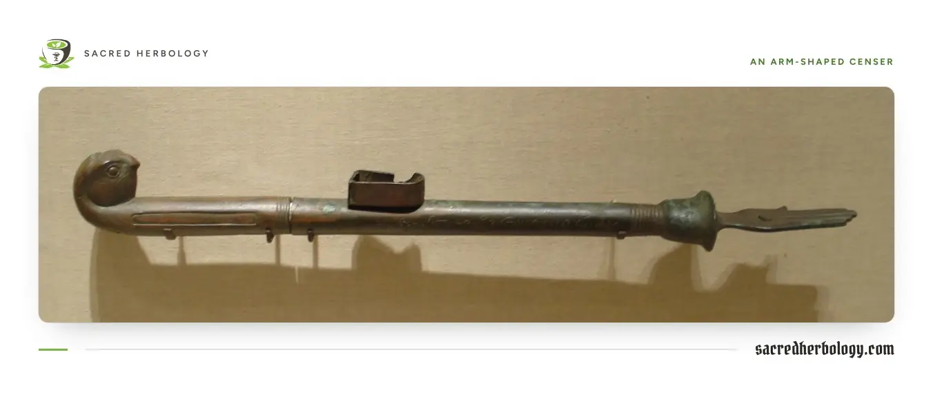 A long bronze censer laid flat: a falcon head at one end, a small lidded box halfway along the shaft, and an open hand at the other end