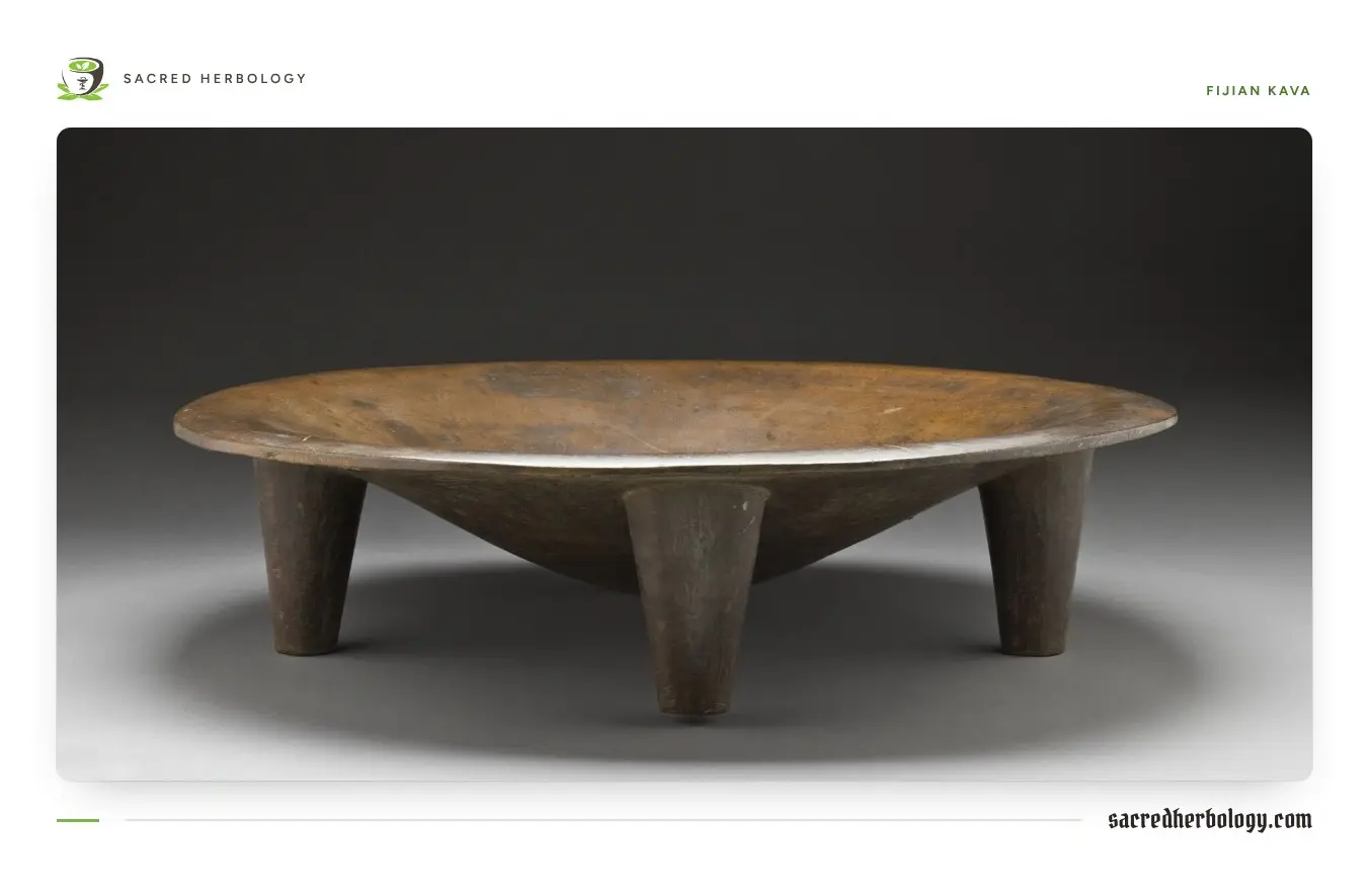 A wide, shallow, dark wooden bowl standing on four short, thick legs, photographed against a grey background