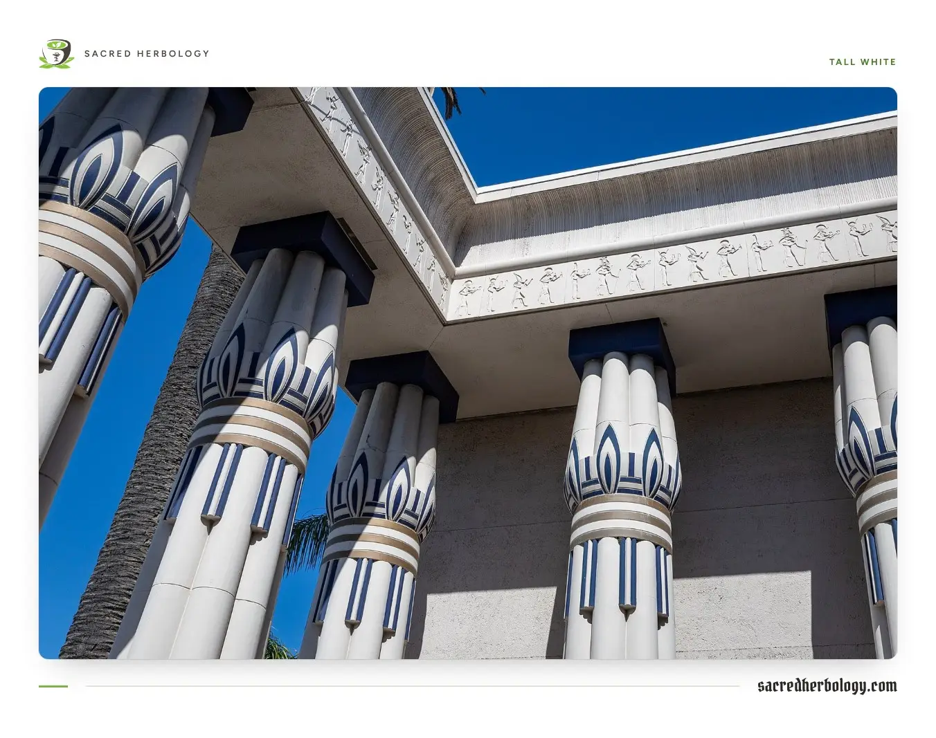 Tall white Egyptian-style columns with lotus-bud capitals in blue and white stripes, under a carved frieze of Egyptian figures, against a deep blue sky